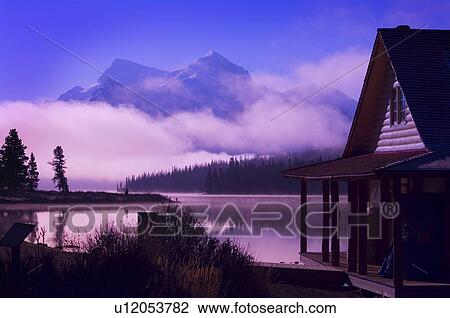 Stock Image - Cabin boathouse and foggy sunrise over mountain lake . Fotosearch