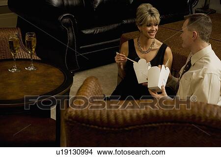 Picture - Couple eating take out in the living room. Fotosearch