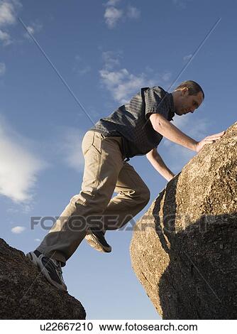 Stock Image - Man climbing up rocks. Fotosearch