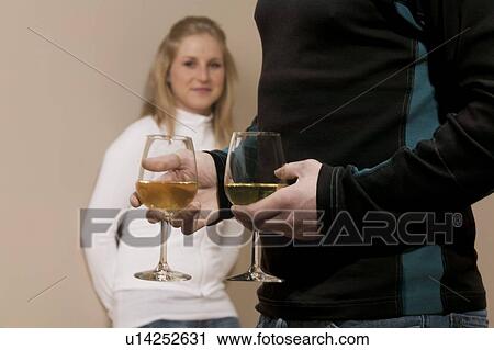 Man holding two wine glasses with woman in background View Large Photo Image Stock Image - Man holding two wine glasses with woman in background. Fotosearch