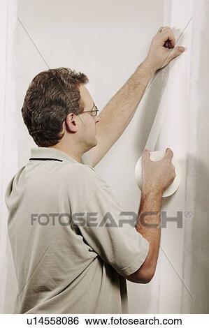 Stock Photograph - Man putting adhesive tape on a wall. Fotosearch