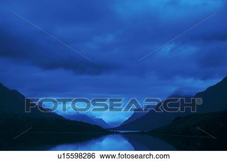 Stock Photograph - Mountains with dark cloud cover over a lake. Fotosearch