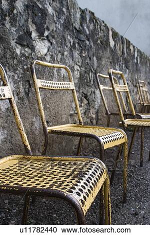 Stock Image - Old metal chairs along a stone wall. Fotosearch
