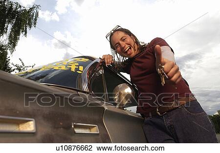 Low angle view of a girl giving thumbs up while leaning on car View Large Photo Image Stock Image - Low angle view of a girl giving thumbs up while leaning on car. Fotosearch