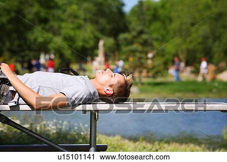 Man laying on a bench near a pond View Large Photo Image Stock Image - Man laying on a bench near a pond. Fotosearch