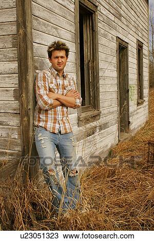 Stock Image - Man leaning against a farm structure. Fotosearch