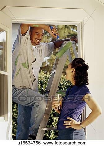 Stock Photograph - Man taking a break from painting the outside of his house. Fotosearch