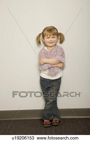 Stock Image - Smiling little girl leaning against a wall with arms crossed. Fotosearch