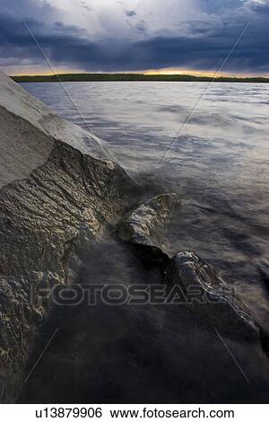 Stock Photograph - Water meeting rock face on lake. Fotosearch