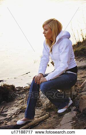 Stock Photo - Woman sitting on rock at a beach. Fotosearch