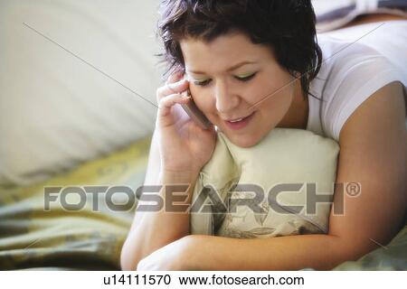 Stock Image - Woman using mobile phone on bed. Fotosearch