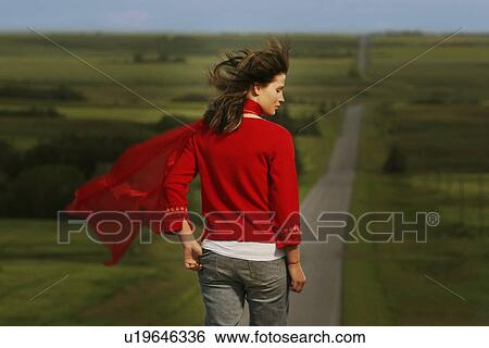 Stock Photograph - Woman walking on road surrounded by fields. Fotosearch