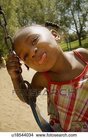 Picture - Young girl sticking out her tongue while on the swing set at the park. Fotosearch