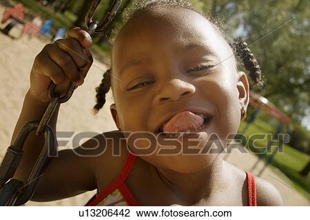 Stock Image - Young girl sticking out her tongue while on the swingset in the park. Fotosearch