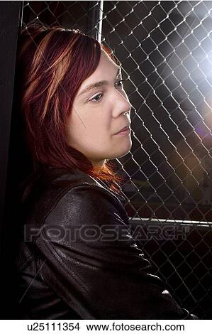 Picture - Young woman standing along chain link fence. Fotosearch