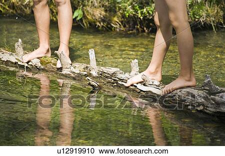 Stock Image - Children standing on a log in a stream. Fotosearch