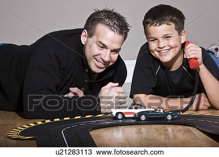 Stock Image - Father and son playing with toy race track. Fotosearch