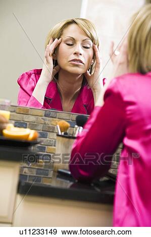 Stock Photo - Woman massaging her head in mirror. Fotosearch