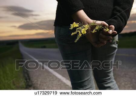 Stock Photo - Woman standing at the side of the road with wild flowers. Fotosearch