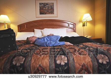 A man laying on a bed in a hotel room View Large Photo Image Stock Photo - A man laying on a bed in a hotel room. Fotosearch