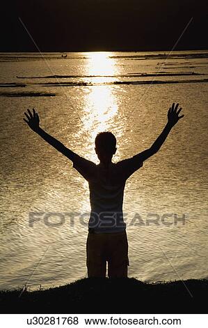 Stock Photo - Child stretching arms to the sky at river bank. Fotosearch