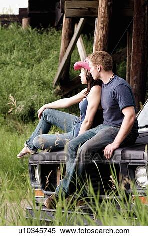 Couple sitting on the hood of a vehicle View Large Photo Image Stock Photography - Couple sitting on the hood of a vehicle. Fotosearch