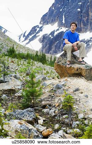 Stock Image - Front view of a man sitting on rock. Fotosearch