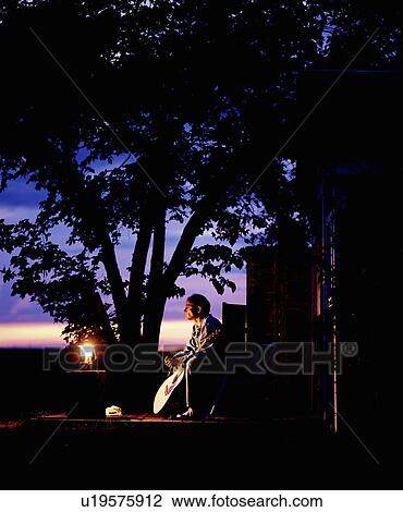 Man sitting with guitar by lantern at dusk View Large Photo Image Stock Image - Man sitting with guitar by lantern at dusk. Fotosearch