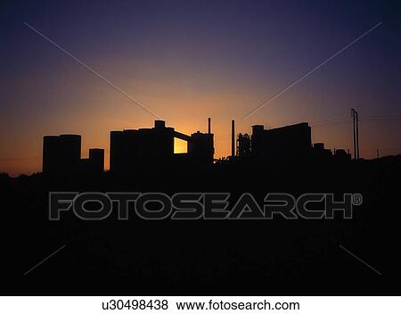 Stock Photo - Concrete factory silhouette, backlit by the sun on the horizon. Fotosearch