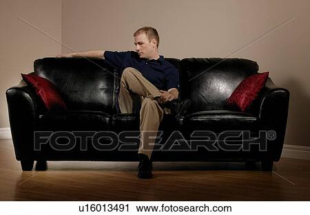 Stock Image - Man sitting on couch alone. Fotosearch