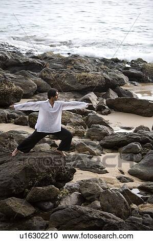 Stock Image - A man stretching on a rocky beach in Koh Lanta, Thailand. Fotosearch