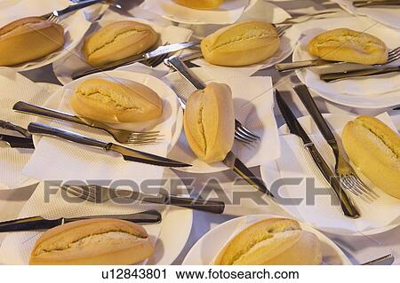 Stock Image - Bread rolls, forks, knives, on plates on a table. Fotosearch