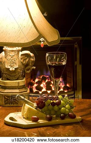 Stock Image - Cheese, grapes and glass of wine on table by lamp. Fotosearch