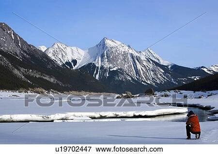 Stock Photo - Man taking a picture of Medicine Lake, Alberta, Canada. Fotosearch