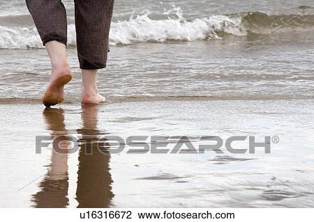 Stock Image - Person walking barefoot on the beach. Fotosearch