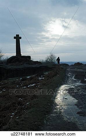 Stock Image - Baslow, Derbyshire, England, United Kingdom; Person walking by a cross monument in a national park. Fotosearch