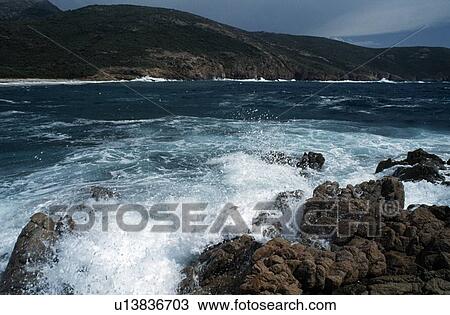 Stock Image - Corsica, France; Waves crashing on a rugged coastline. Fotosearch
