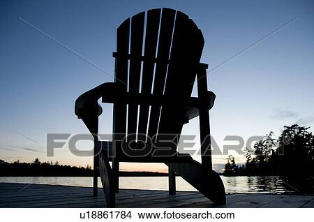 Lake of the Woods, Ontario, Canada; Empty deck chair on a pier next to a lake View Large Photo Image Picture - Lake of the Woods, Ontario, Canada; Empty deck chair on a pier next to a lake. Fotosearch