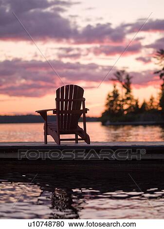Stock Image - Lake of the Woods, Ontario, Canada; Empty deck chair on a pier next to a lake. Fotosearch