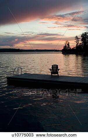Lake of the Woods, Ontario, Canada; Empty deck chair on a pier next to a lake View Large Photo Image Stock Image - Lake of the Woods, Ontario, Canada; Empty deck chair on a pier next to a lake. Fotosearch