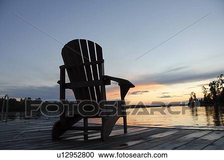 Lake of the Woods, Ontario, Canada; Empty deck chair on a pier next to a lake View Large Photo Image Stock Image - Lake of the Woods, Ontario, Canada; Empty deck chair on a pier next to a lake. Fotosearch