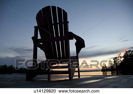 Stock Image - Lake of the Woods, Ontario, Canada; Empty deck chair on a pier next to a lake. Fotosearch