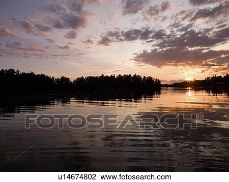 Stock Image - Lake of the Woods, Ontario, Canada; Sunrise over lake. Fotosearch