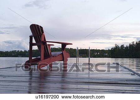Stock Image - Lake of the Woods, Ontario, Canada; Empty deck chair on a pier next to a lake. Fotosearch