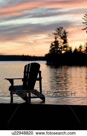 Stock Image - Lake of the Woods, Ontario, Canada; Empty deck chair on a pier next to a lake. Fotosearch
