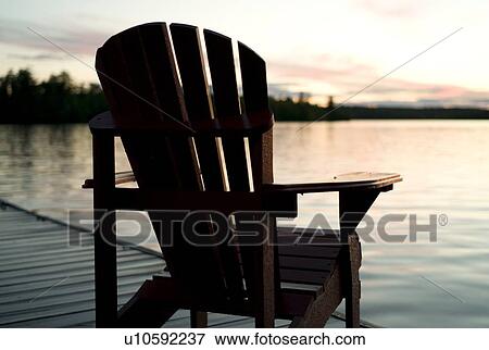 Lake of the Woods, Ontario, Canada; Empty deck chair on a pier next to a lake View Large Photo Image Stock Photo - Lake of the Woods, Ontario, Canada; Empty deck chair on a pier next to a lake. Fotosearch