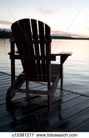 Stock Photo - Lake of the Woods, Ontario, Canada; Empty deck chair on a pier next to a lake. Fotosearch