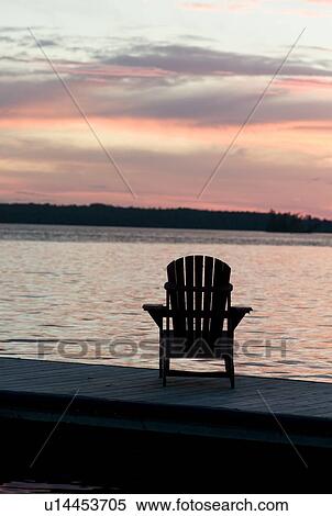 Lake of the Woods, Ontario, Canada; Empty deck chair on a pier next to a lake View Large Photo Image Stock Photography - Lake of the Woods, Ontario, Canada; Empty deck chair on a pier next to a lake. Fotosearch