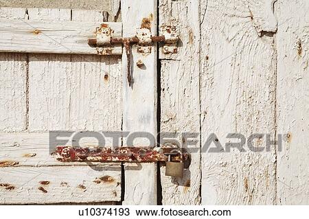 Stock Image - Rusted lock and bolt on a weathered wooden door. Fotosearch