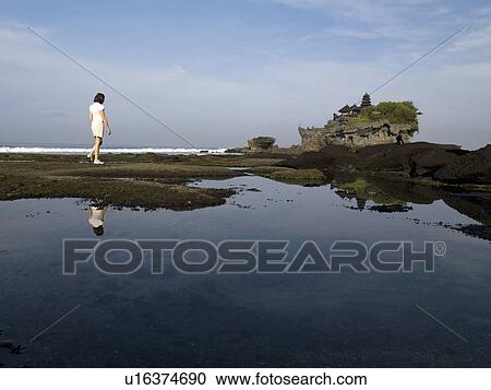 Stock Image - Tanah Lot Sea Temple, Bali, Indonesia; Woman walking along the shore. Fotosearch